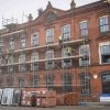 A LISTED BUILDING RENOVATION IN THE UK. The image depicts a Victorian brick warehouse building undergoing a sustainable retrofit, featuring scaffolding and the installation of new windows. This transformation highlights sustainable architecture examples, focusing on energy efficiency and the use of sustainable materials to minimize environmental impact.